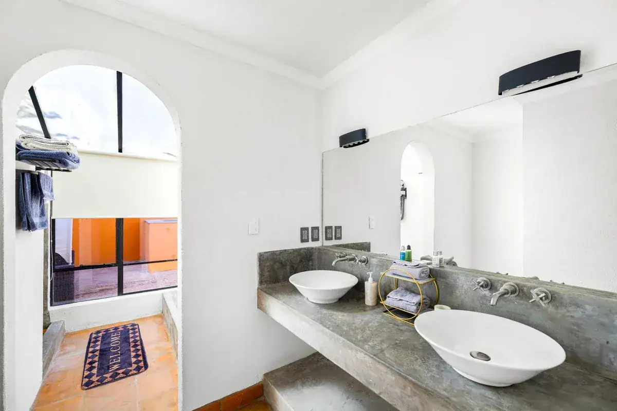 Santo Domingo House, bathroom with a gray concrete counter, two vessel sinks and an arched window, San Miguel de Allende