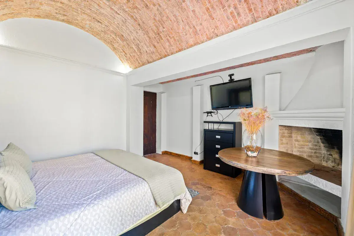 Santo Domingo House, bedroom with a white and gray bed, a dresser with a television and a round wood table, San Miguel de Allende