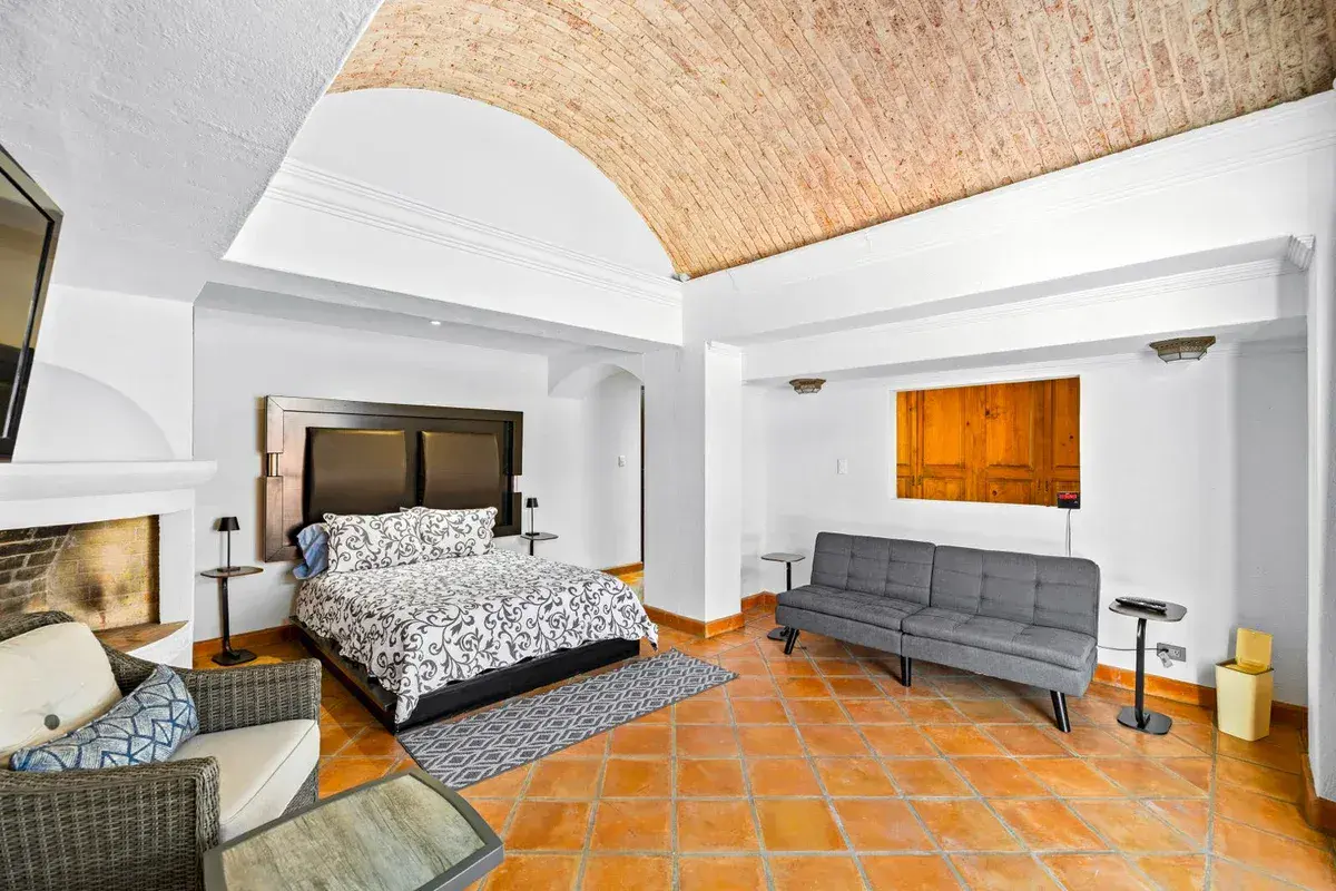 Santo Domingo House, bedroom with a patterned bed, a gray sofa, a fireplace and a brick vaulted ceiling, San Miguel de Allende