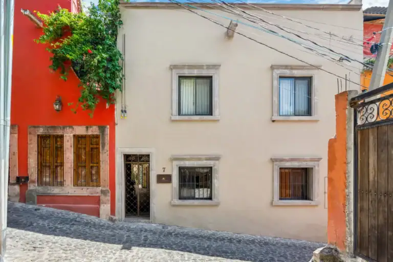 Suites Casa Vistas, pale stucco street facade with stone-framed windows next to a red neighboring house, San Miguel de Allende