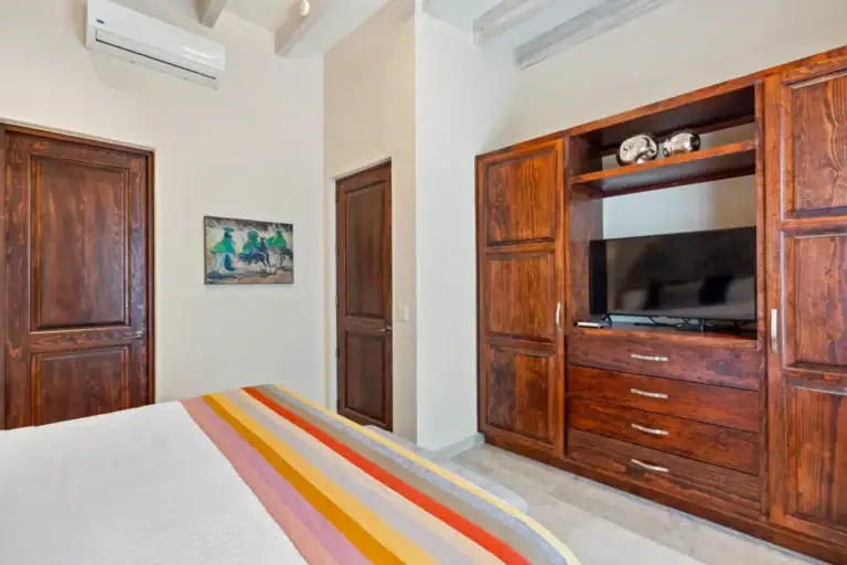 Suites Casa Vistas, bedroom with a striped blanket, built-in wood entertainment cabinet and a wall-mounted air conditioner, San Miguel de Allende