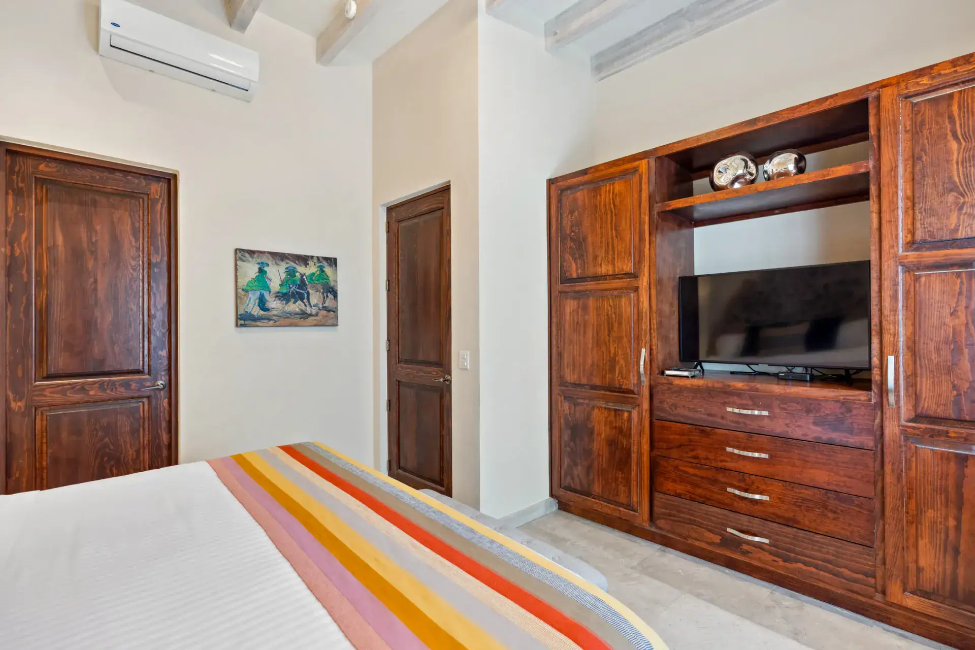 Suites Casa Vistas, bedroom with a striped blanket, built-in wood entertainment cabinet and a wall-mounted air conditioner, San Miguel de Allende