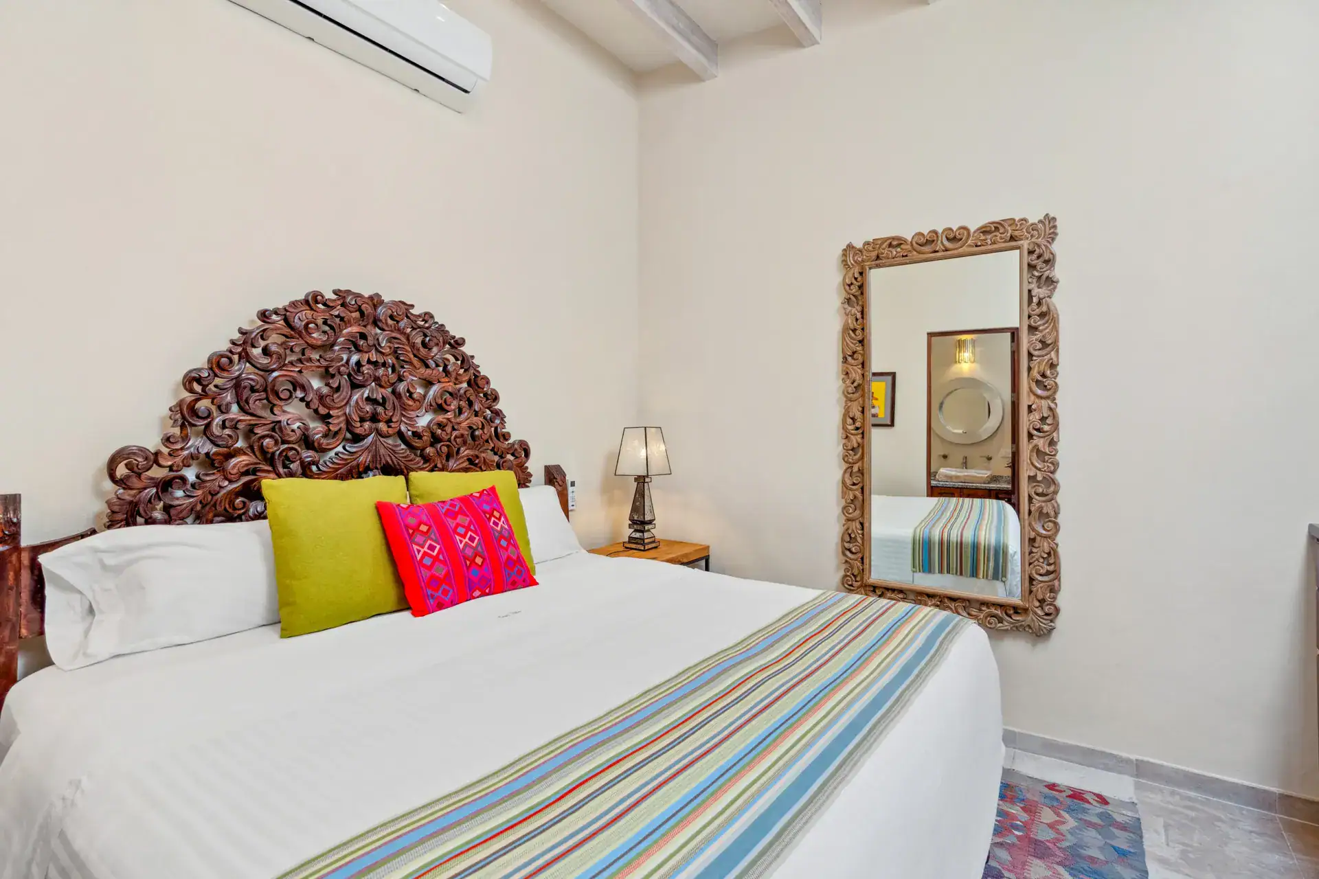 Suites Casa Vistas, bedroom with a carved wood headboard, colorful pillows and a tall mirror, San Miguel de Allende