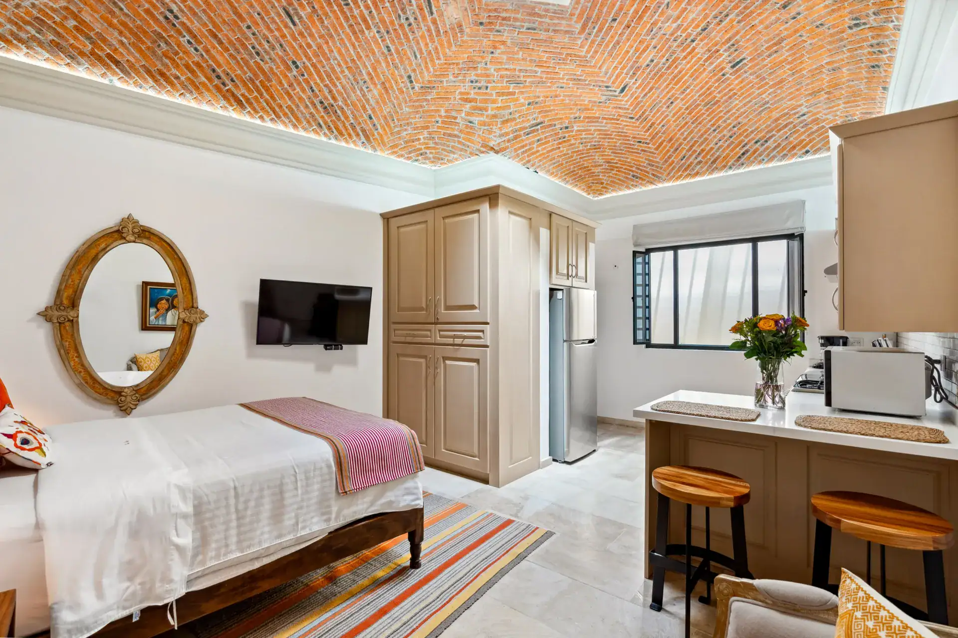 Suites Casa Vistas, studio suite with a bed, an oval mirror, a television, a kitchen island and bar stools under a brick vaulted ceiling, San Miguel de Allende