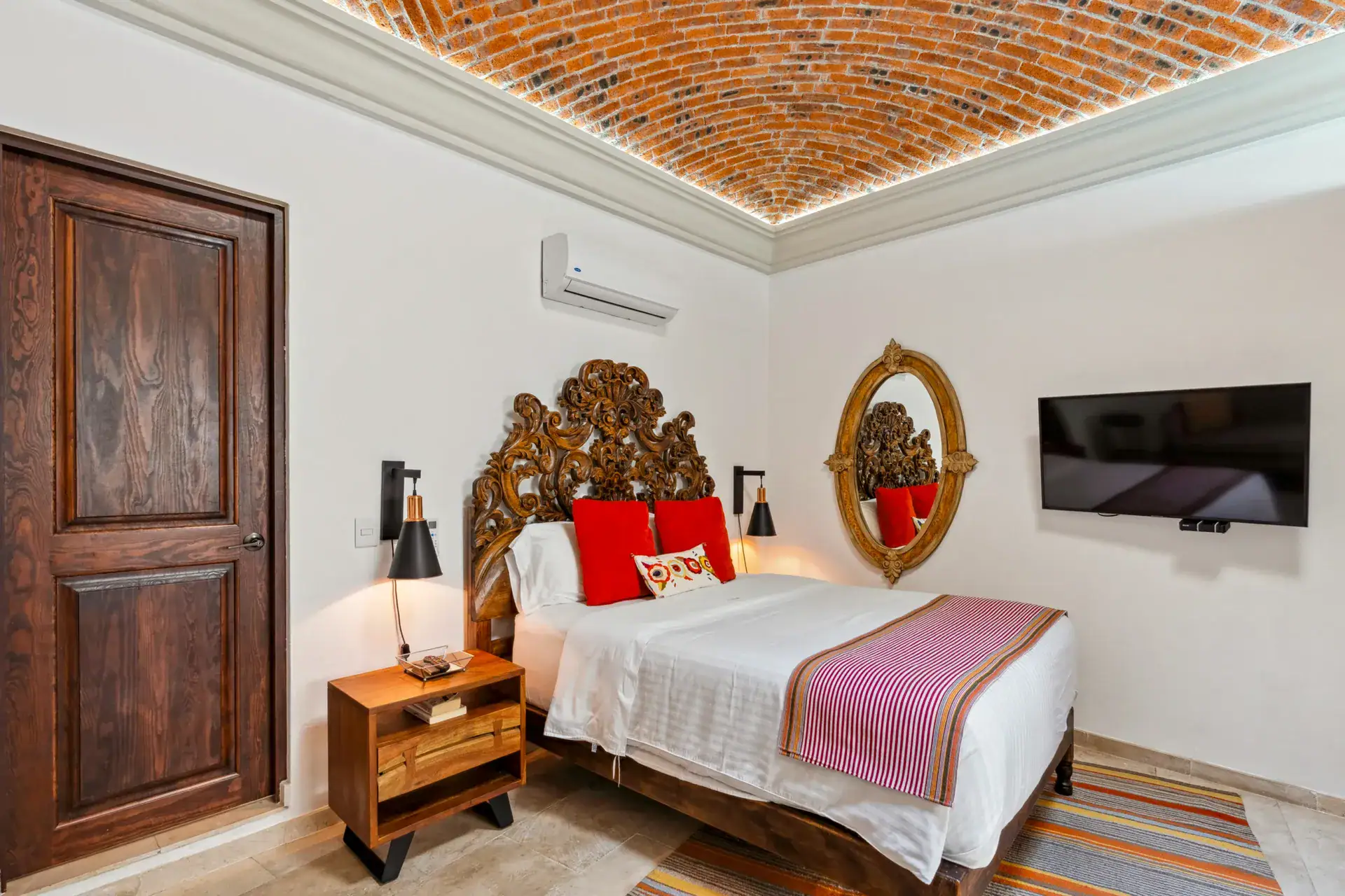 Suites Casa Vistas, bedroom with a carved headboard, red accent pillows and a brick vaulted ceiling, San Miguel de Allende