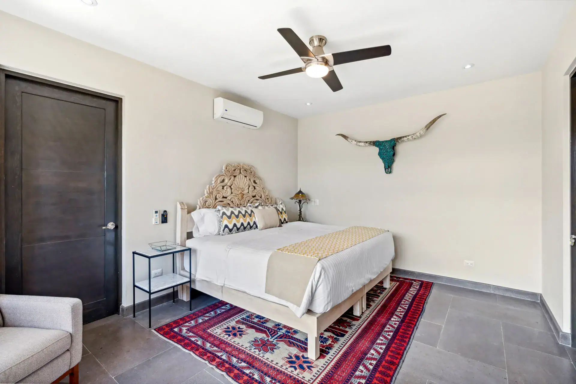 Suites Casa Vistas, bedroom with a carved headboard, red rug, longhorn skull and wall-mounted air conditioner, San Miguel de Allende