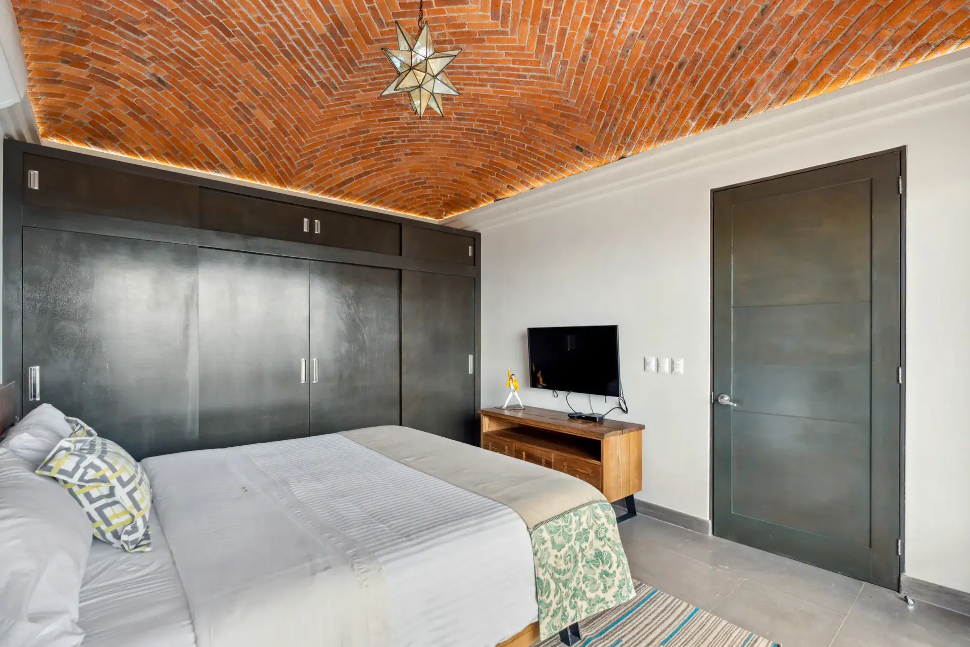 Suites Casa Vistas, bedroom with a dark wood wardrobe, television and a brick vaulted ceiling with a star lantern, San Miguel de Allende