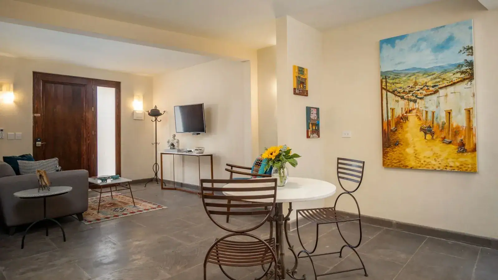 Suites Casa Vistas, ground-floor suite with a sofa, small dining table, television and a large painting of a village street, San Miguel de Allende