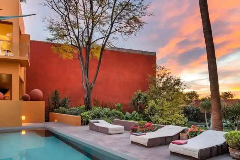 Contemporary home with orange and red walls, a plunge pool and lounge chairs under a sunset sky
