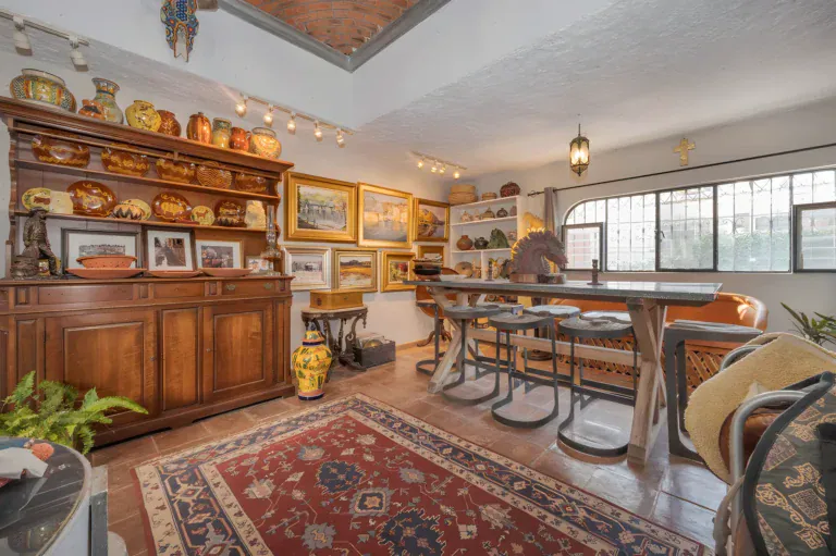 Two Homes, great room with a large wood hutch of pottery, a wood bar table with stools and a red Persian rug, San Miguel de Allende