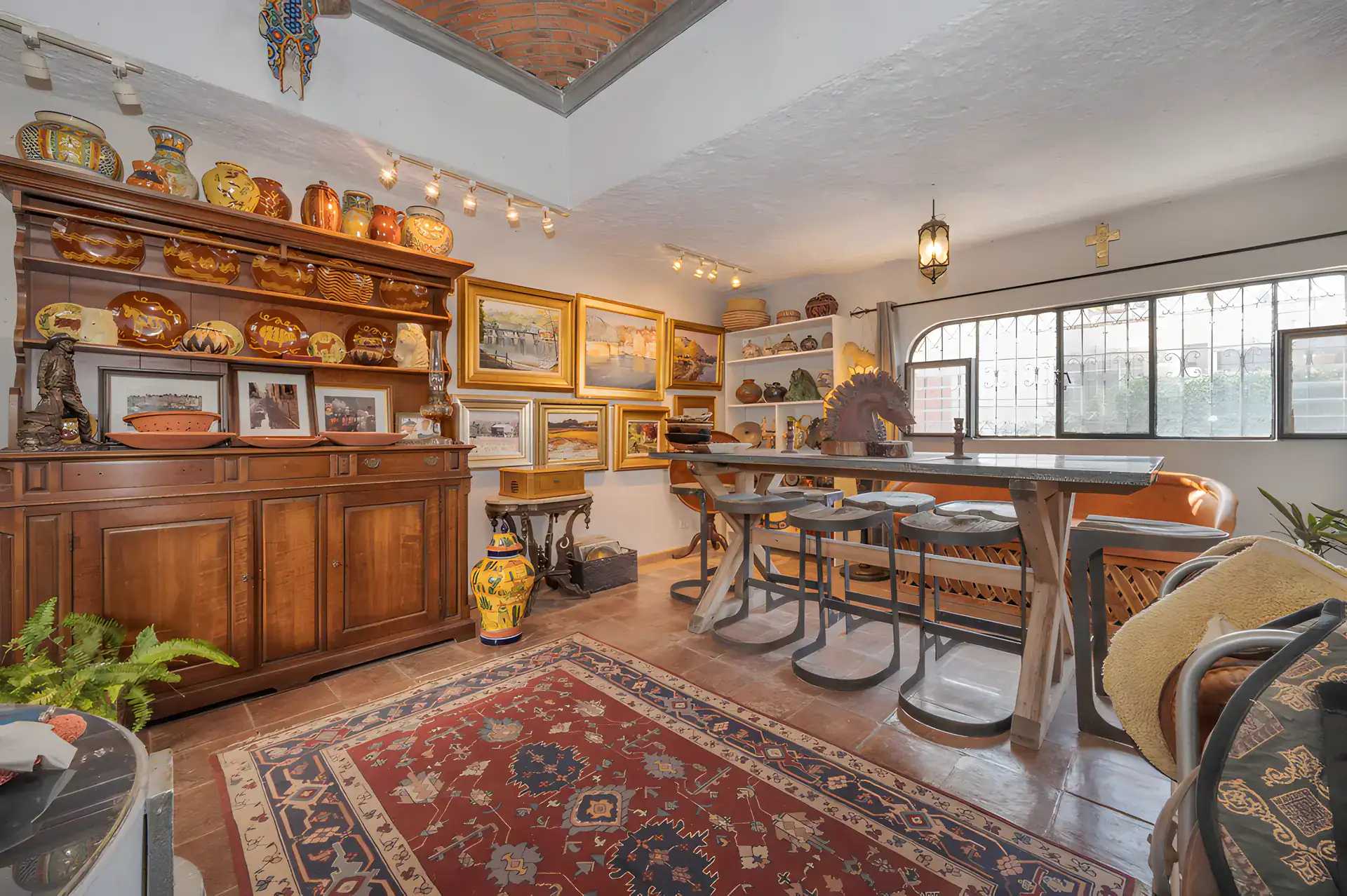 Two Homes, great room with a large wood hutch of pottery, a wood bar table with stools and a red Persian rug, San Miguel de Allende