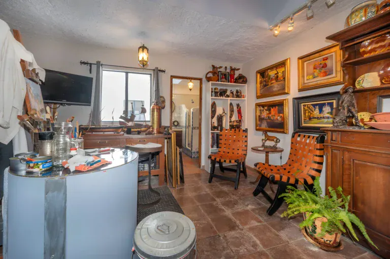 Two Homes, artist's studio with a round blue table, two woven leather chairs and shelves of art objects, San Miguel de Allende