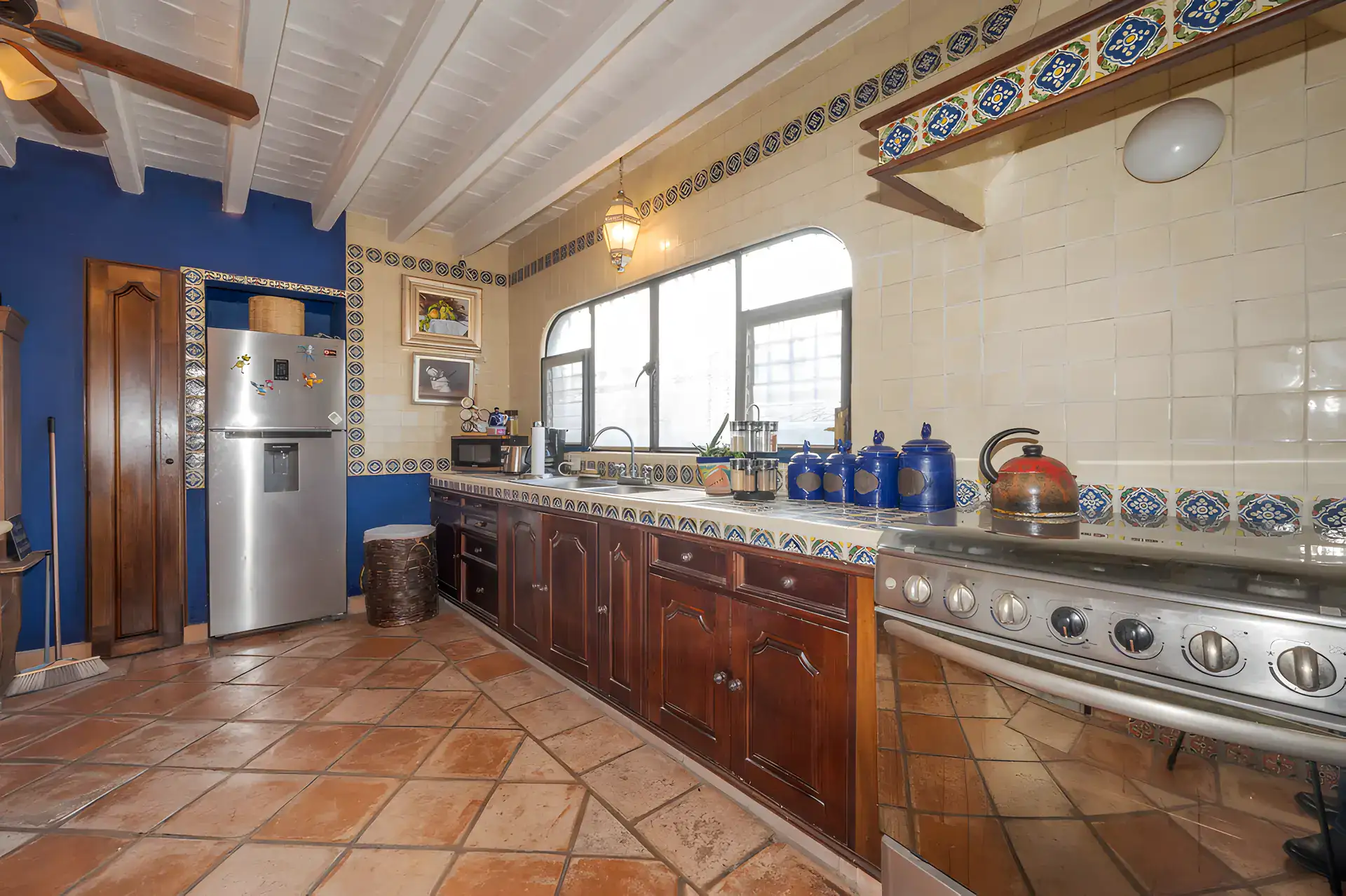 Two Homes, kitchen with a stainless refrigerator, a stainless range and blue and white tiles under a white beamed ceiling, San Miguel de Allende