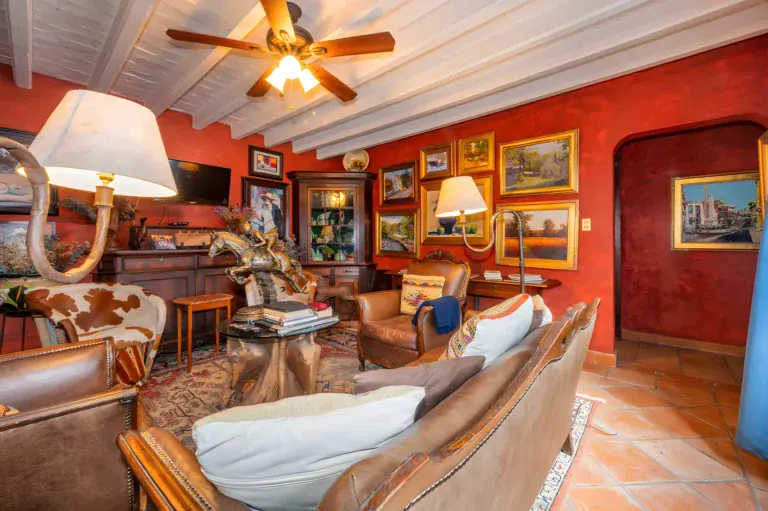 Two Homes, living room with a red wall, leather sofas, a ceiling fan and walls covered in framed paintings, San Miguel de Allende