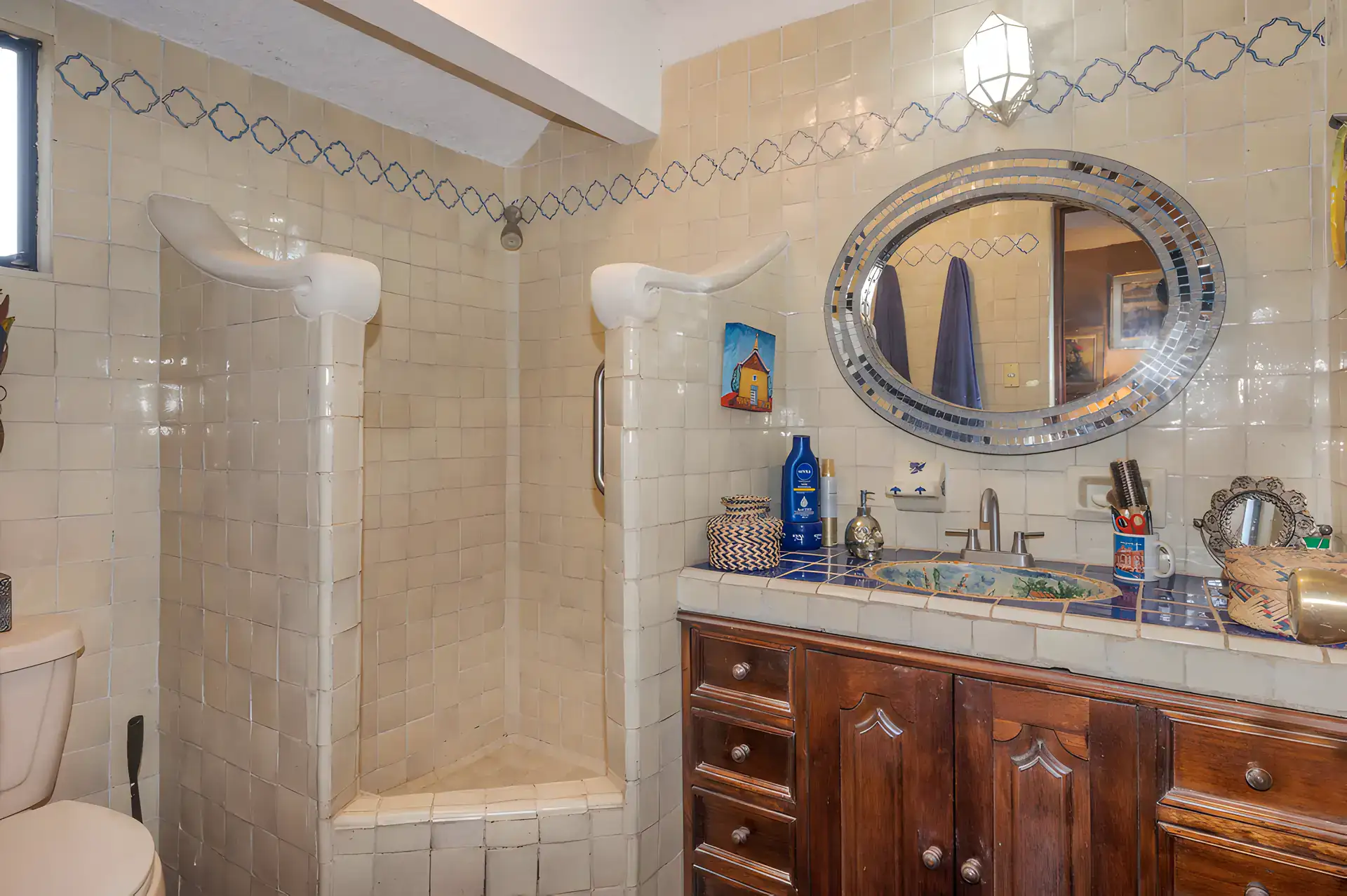 Two Homes, bathroom with a tiled shower, a hand-painted sink, an oval mirror and cream tile walls, San Miguel de Allende