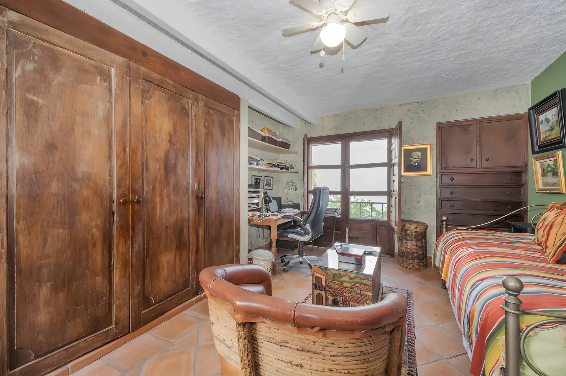 Two Homes, study with built-in wood wardrobes, a desk, a daybed with a striped blanket and glass doors, San Miguel de Allende
