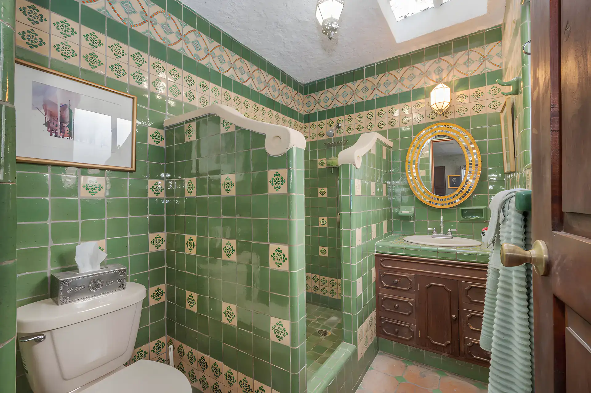 Two Homes, bathroom with green and white tile, a gold round mirror and a tiled shower, San Miguel de Allende