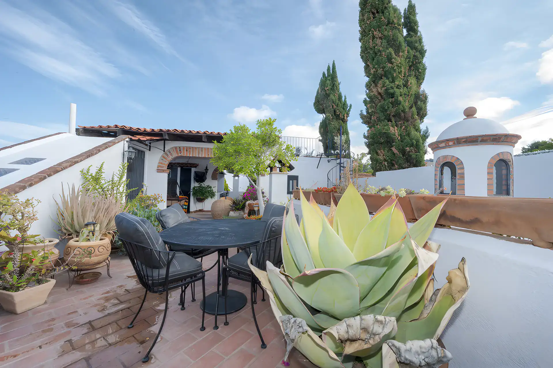 Two Homes, rooftop terrace with a dining table, agaves in pots and white domed structures, San Miguel de Allende