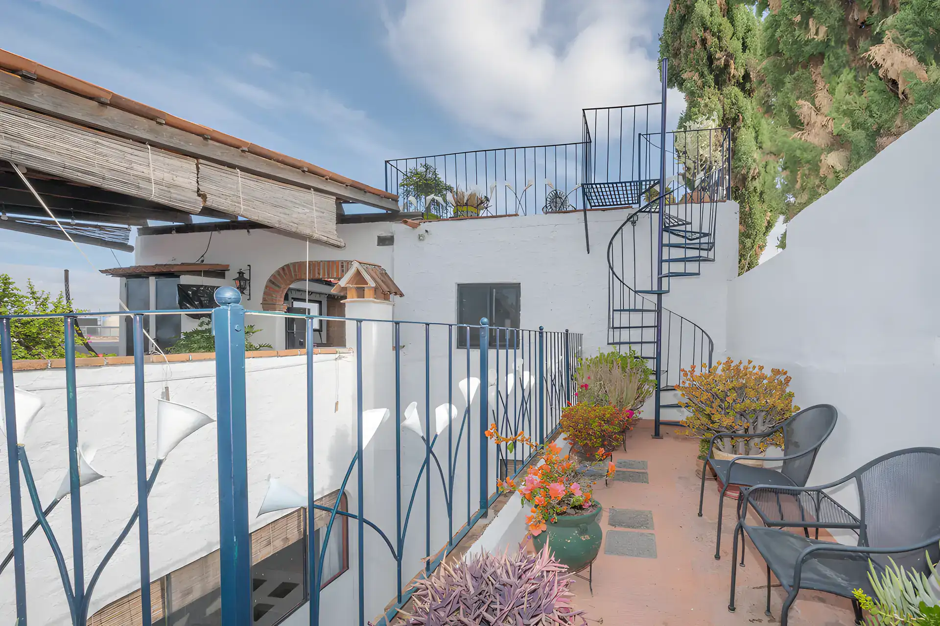 Two Homes, narrow roof terrace with an iron railing, a spiral staircase and potted plants, San Miguel de Allende