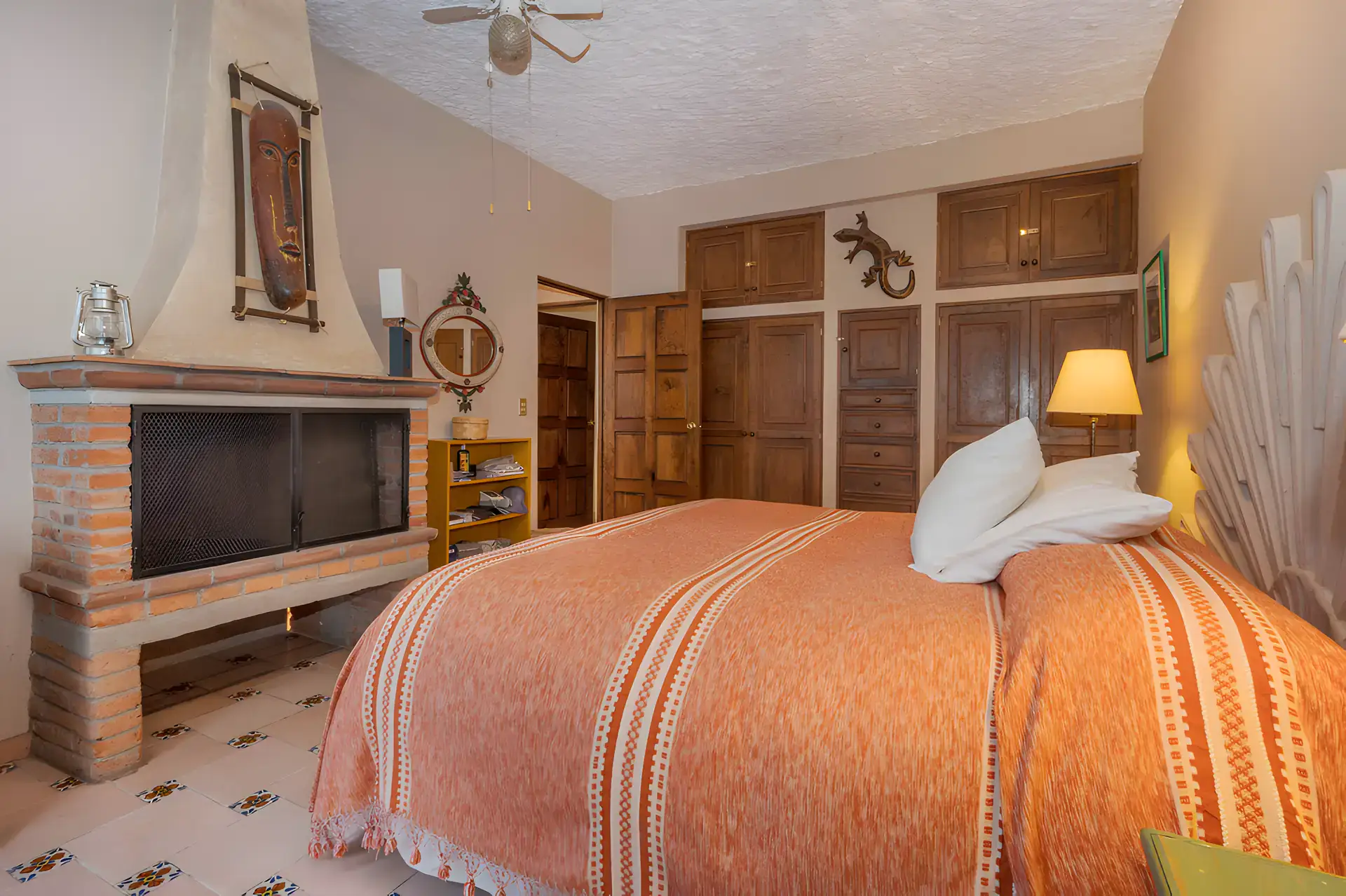 Two Homes, bedroom with a brick fireplace, wood wardrobes and an orange striped bedspread, San Miguel de Allende