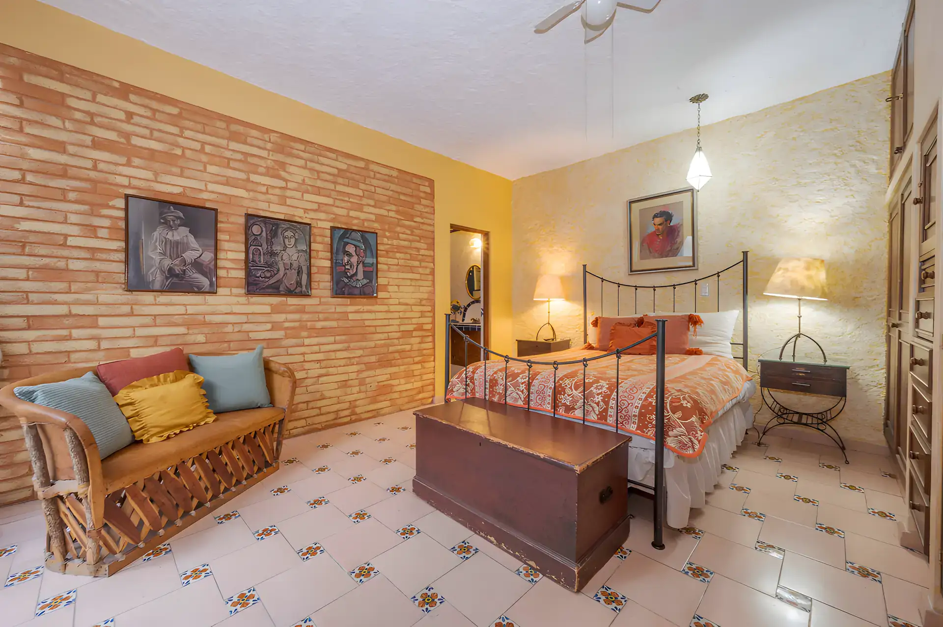 Two Homes, bedroom with a brick feature wall, a wrought-iron bed, an equipale love seat and a wood trunk, San Miguel de Allende