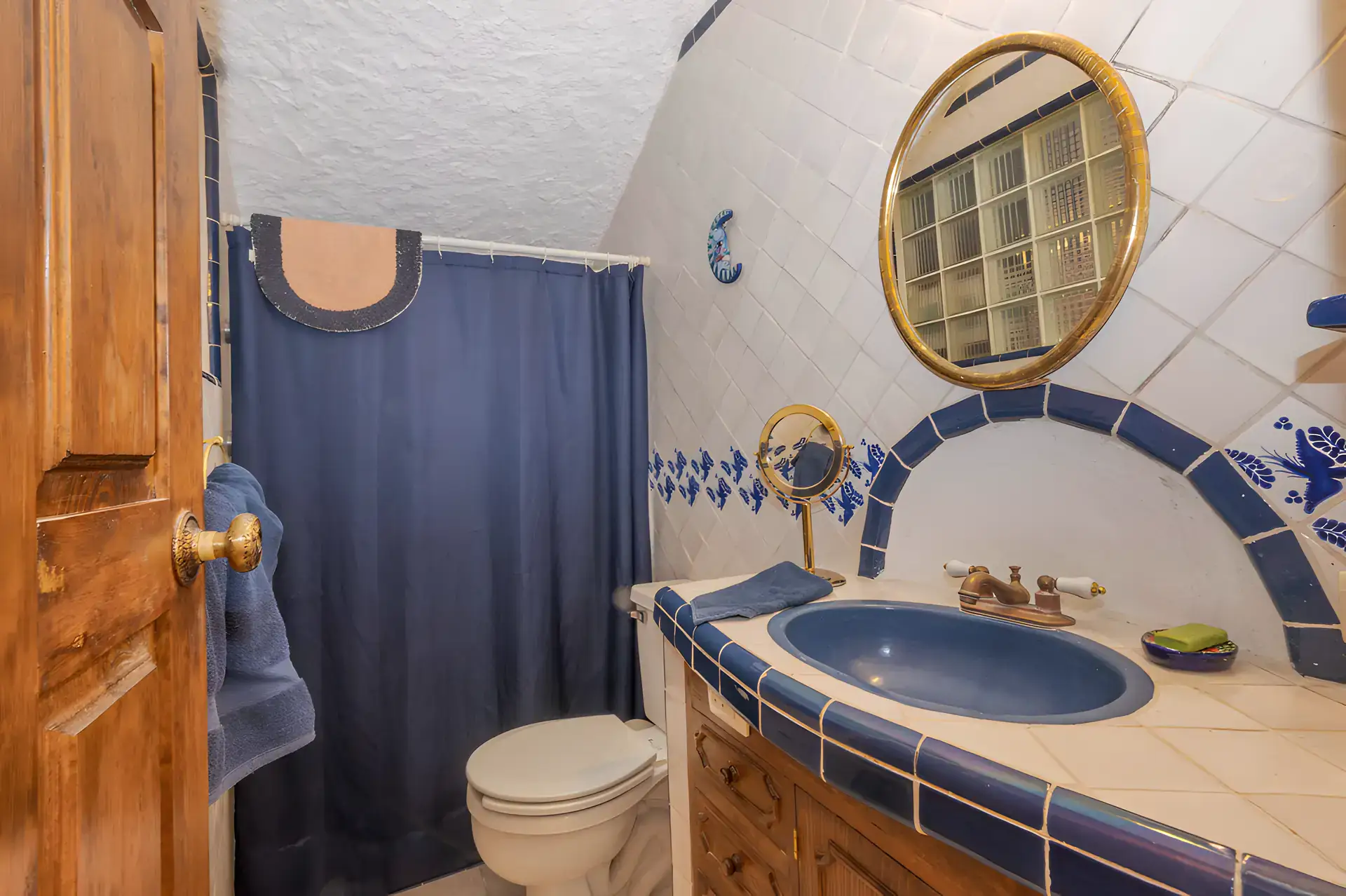 Two Homes, bathroom with a blue tiled sink, a round gold mirror and a navy shower curtain, San Miguel de Allende
