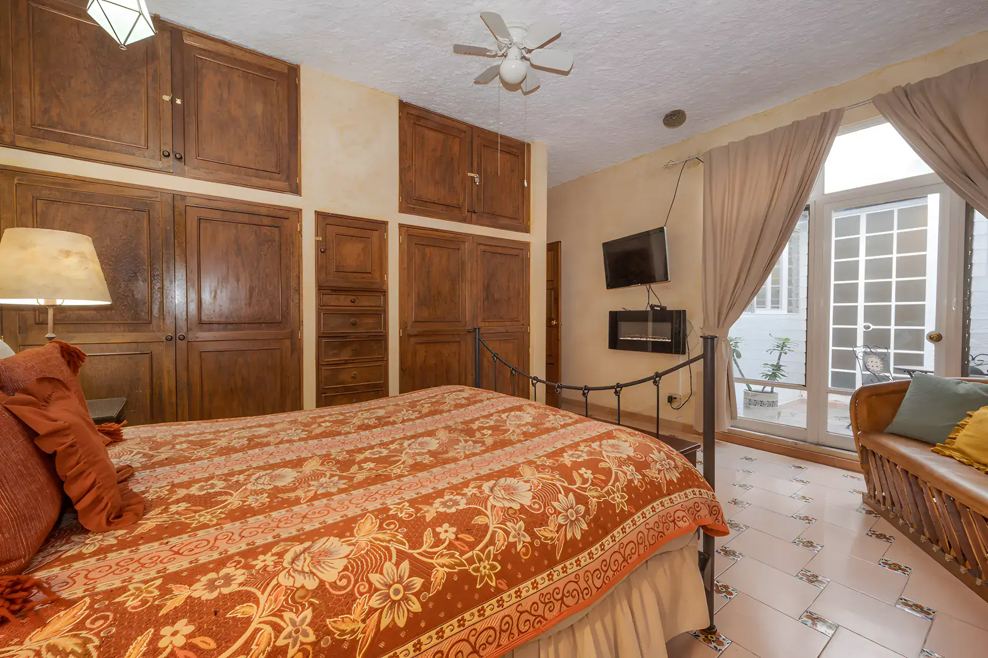 Two Homes, bedroom with wood wardrobes, a patterned bedspread, a television and glass doors to the garden, San Miguel de Allende
