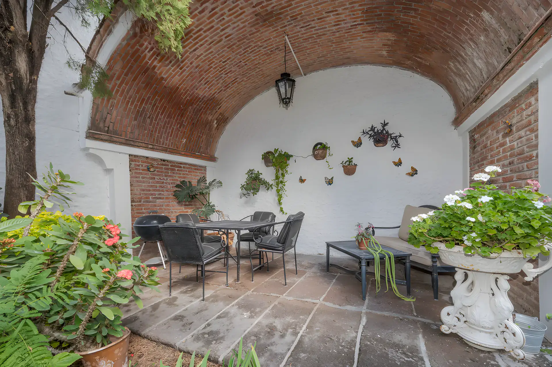 Two Homes, garden patio with a brick vaulted loggia, an outdoor dining set and flowering plants, San Miguel de Allende