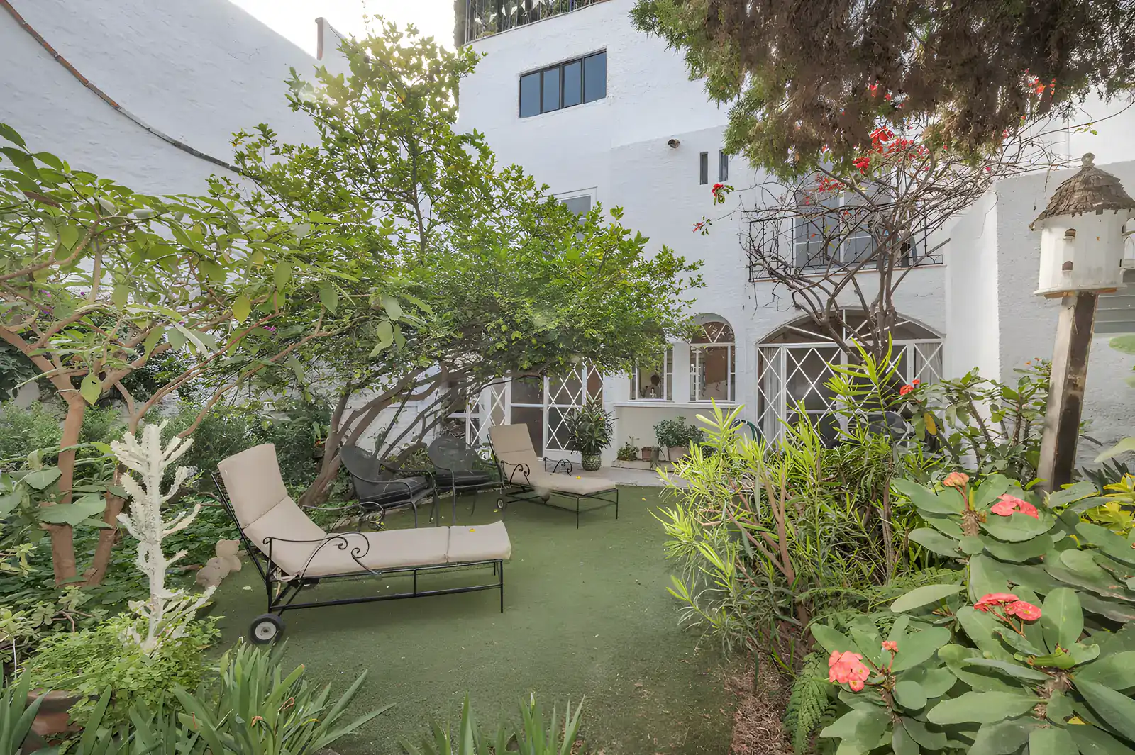 Two Homes, garden lawn with lounge chairs, flower beds, a birdhouse and a view of the buildings, San Miguel de Allende