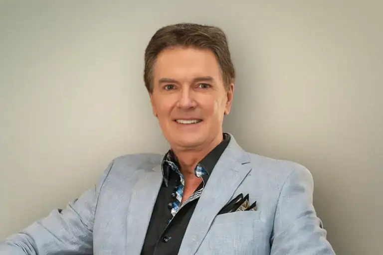 Portrait of Greg Gunter smiling in a light blue linen blazer and black shirt