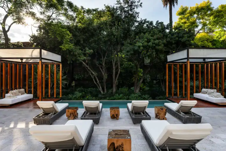 Villa del Parque Central, pool with lounge chairs and two wood-slat cabanas surrounded by trees, San Miguel de Allende