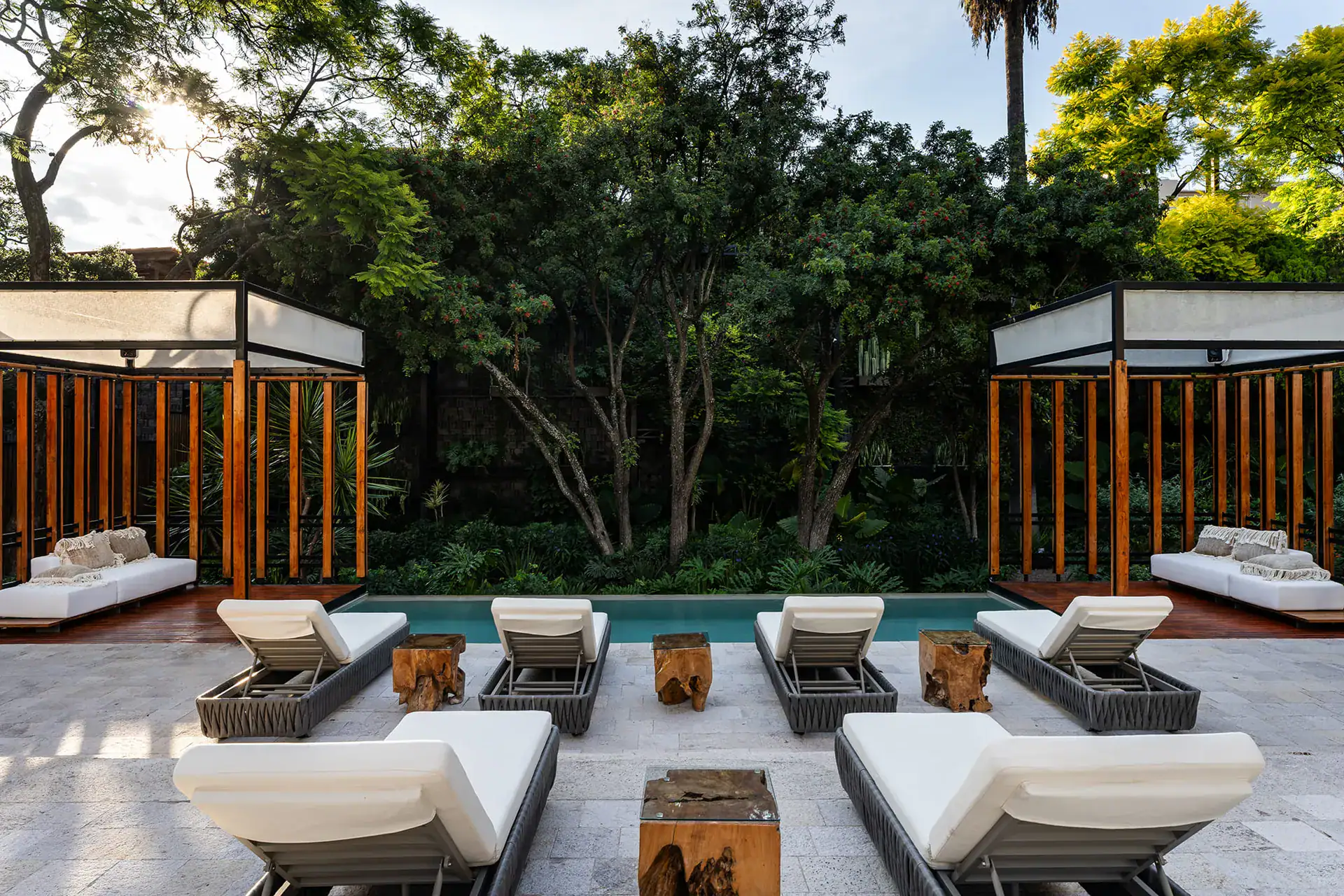 Villa del Parque Central, pool with lounge chairs and two wood-slat cabanas surrounded by trees, San Miguel de Allende