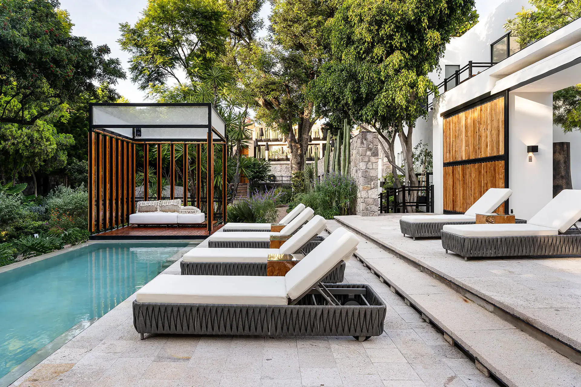Villa del Parque Central, row of lounge chairs beside the infinity pool with a cabana daybed and wood-slat screen, San Miguel de Allende