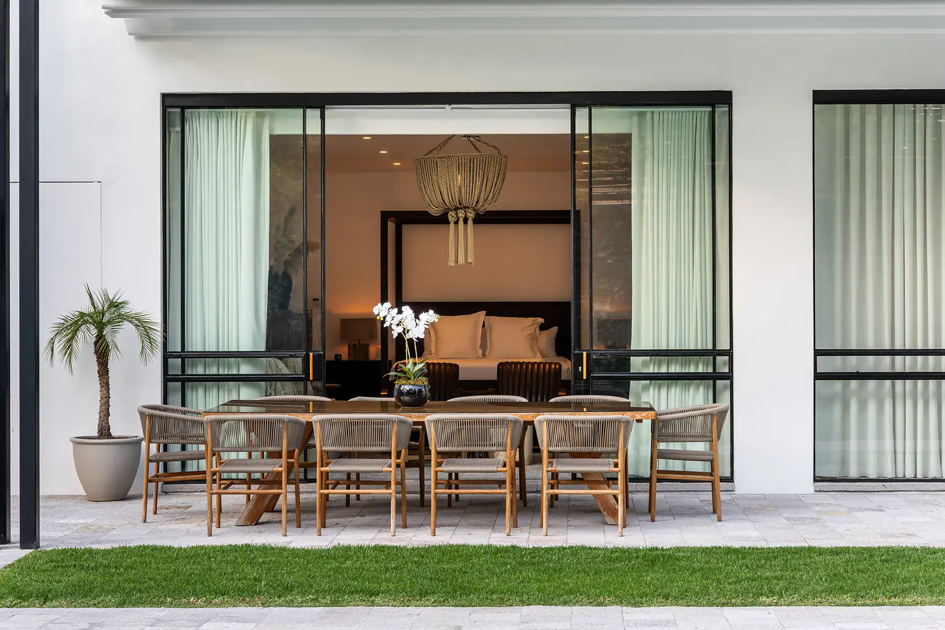 Villa del Parque Central, outdoor dining table for ten in front of a glass-walled bedroom with a hanging light, San Miguel de Allende