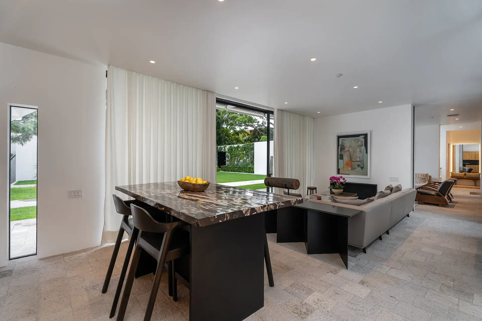 Villa del Parque Central, living and dining area with a stone-topped table, gray sofa and sliding glass walls opening to the lawn, San Miguel de Allende