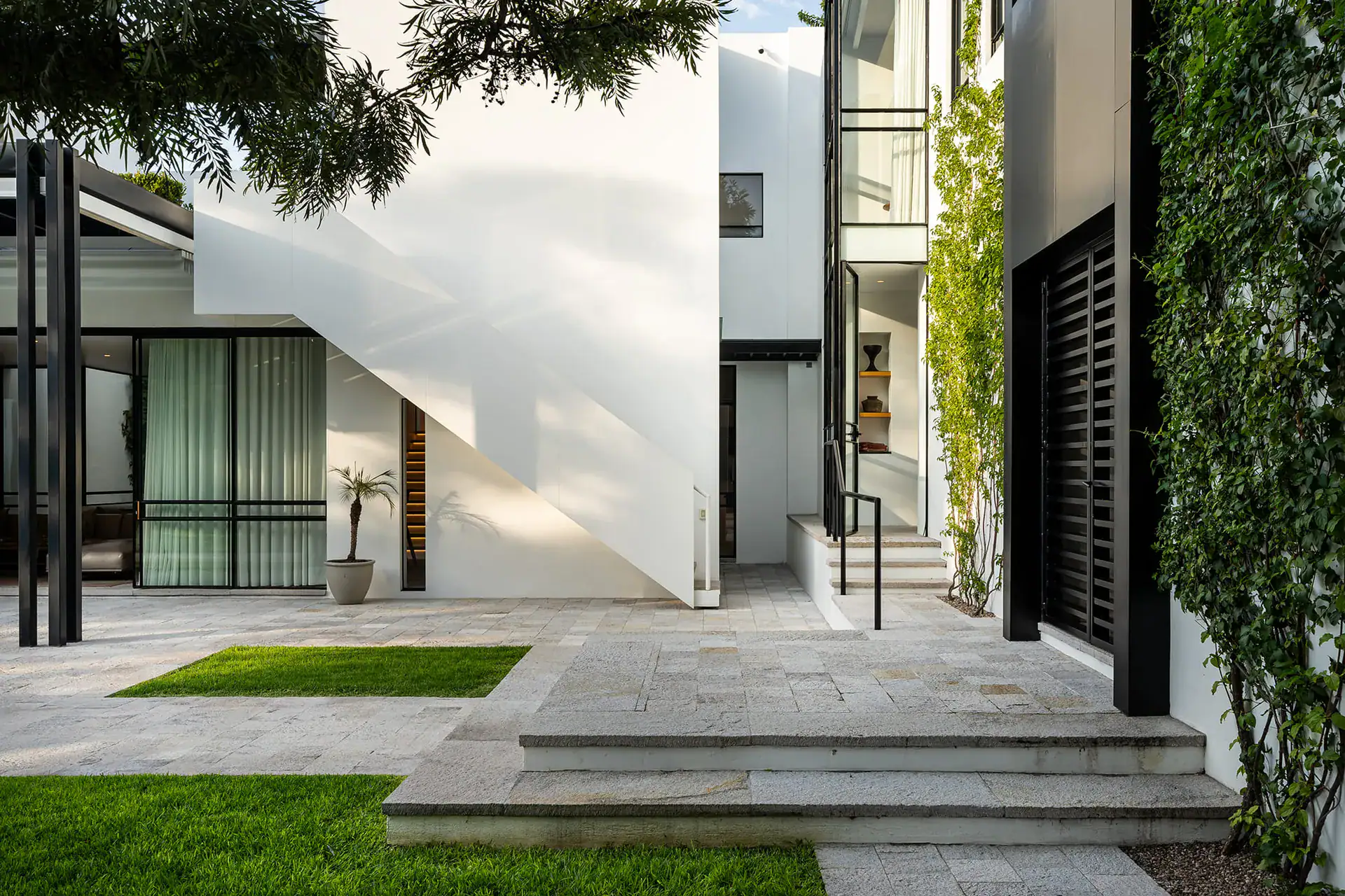 Villa del Parque Central, courtyard with lawn, stone steps and a white exterior staircase beside a green wall, San Miguel de Allende