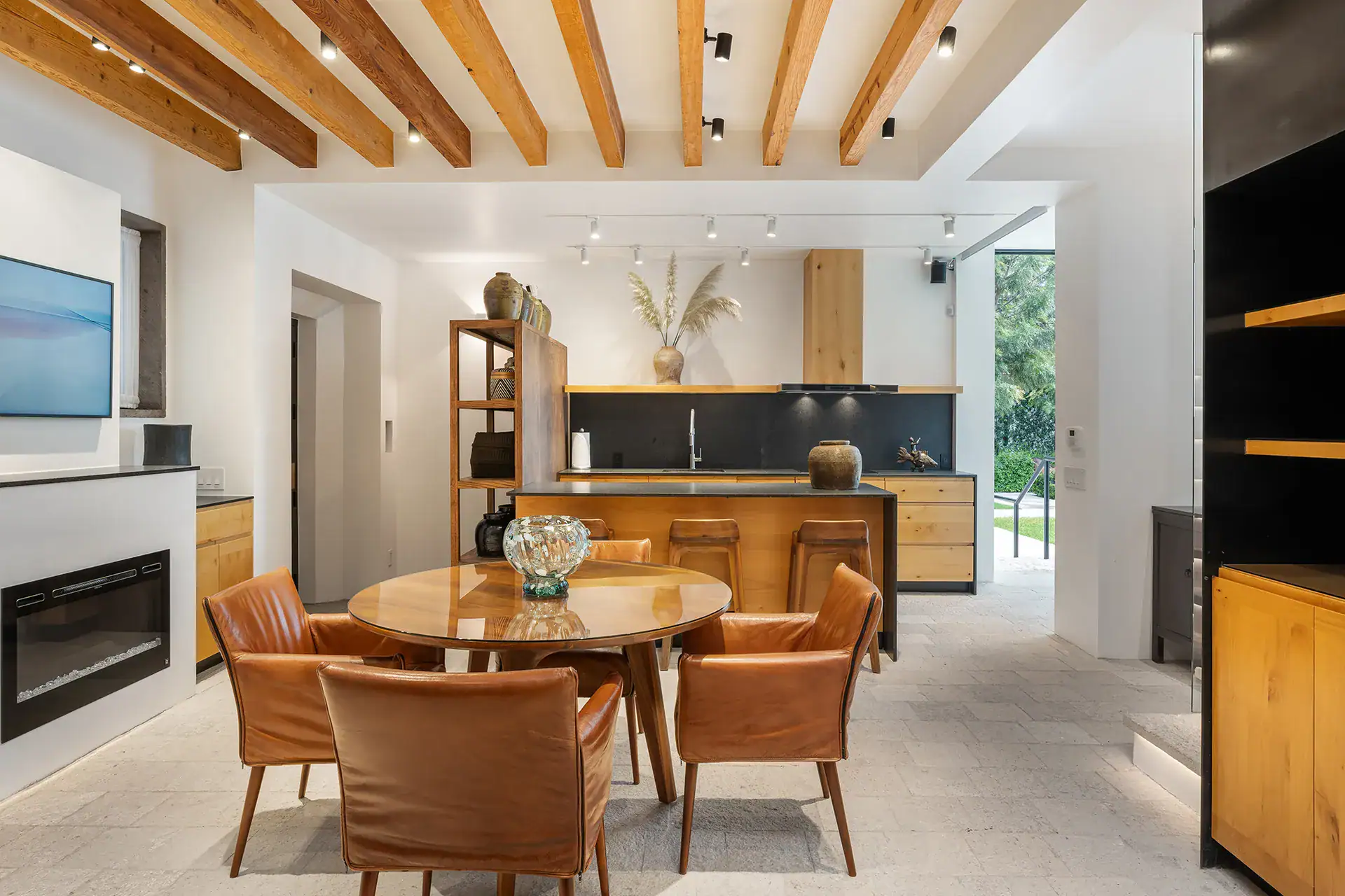 Villa del Parque Central, dining area with a round table and leather chairs beside an open kitchen and fireplace under beamed ceilings, San Miguel de Allende