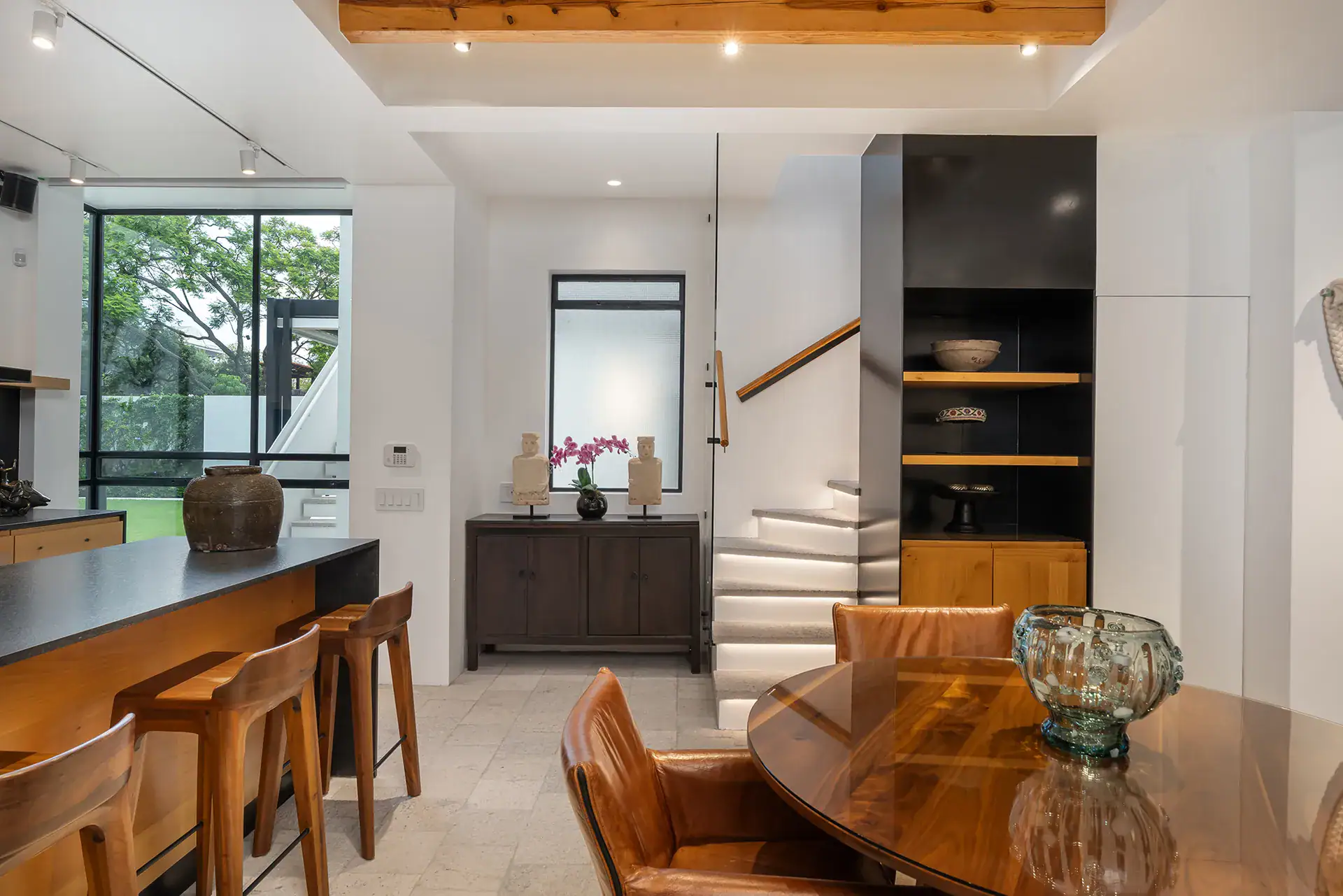 Villa del Parque Central, dining table and kitchen island beside a staircase and a window onto the garden, San Miguel de Allende