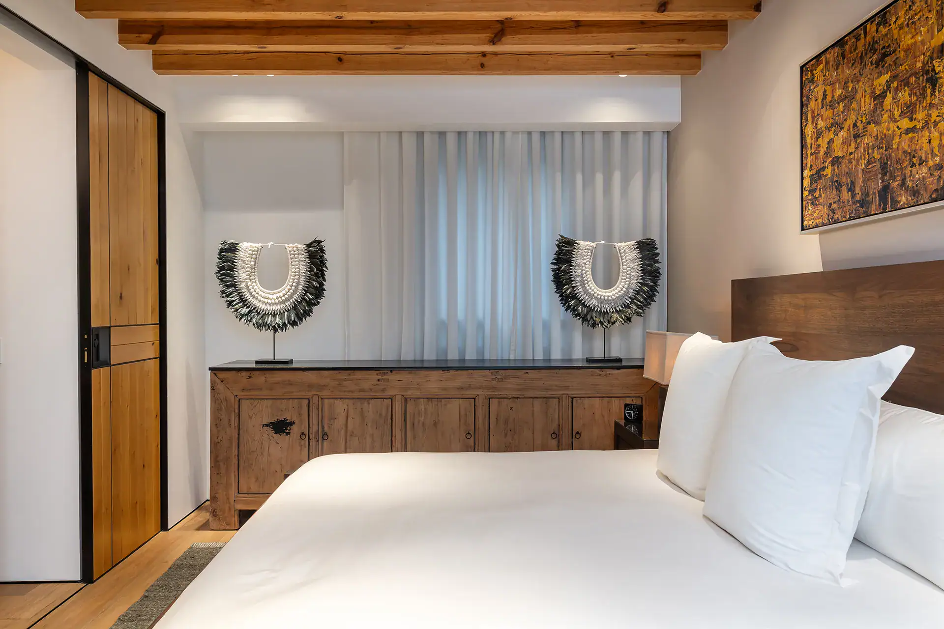 Villa del Parque Central, bed with white pillows, carved sideboard and woven decorative pieces under a beamed ceiling, San Miguel de Allende