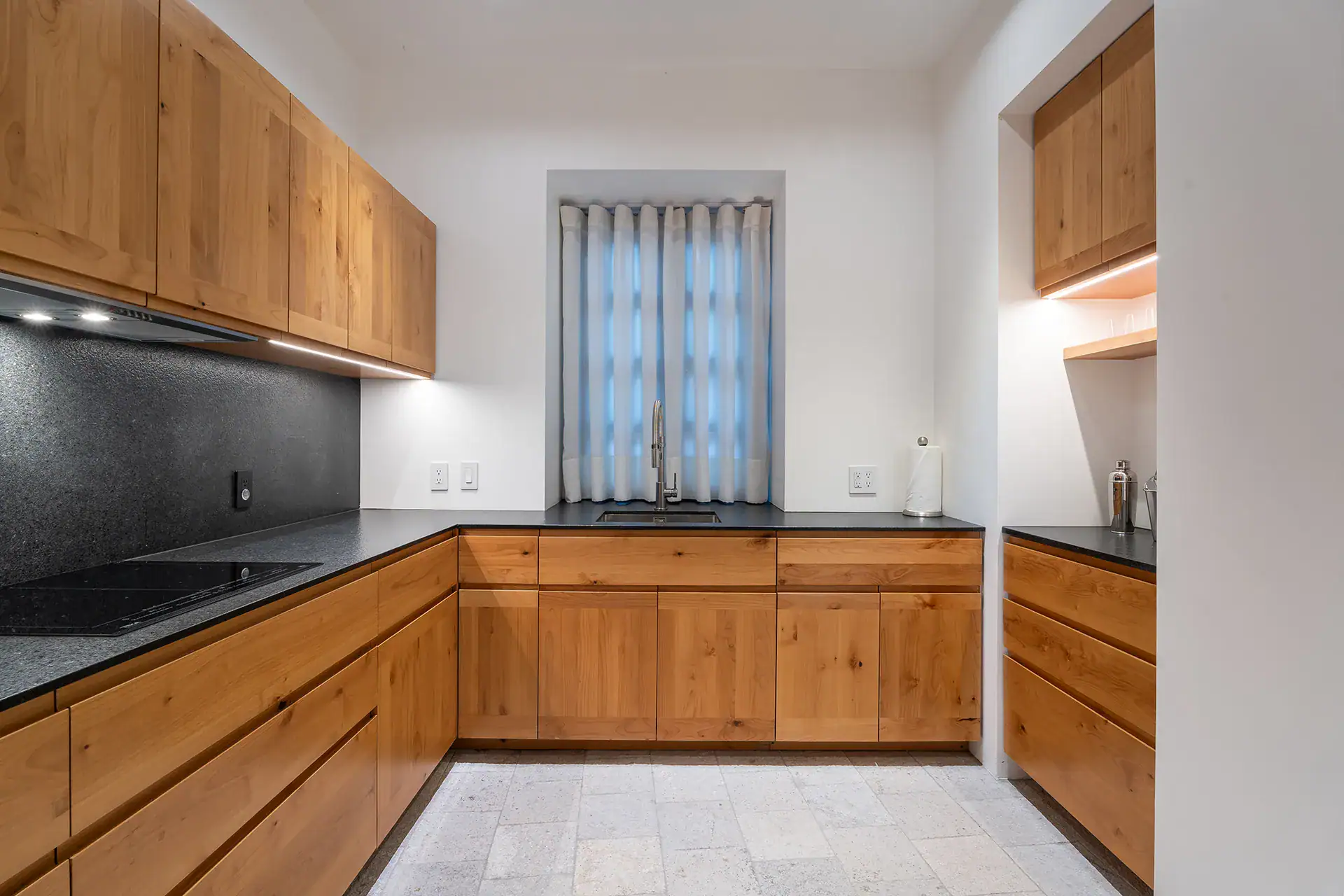 Villa del Parque Central, kitchen with oak cabinets, black counters and a window with sheer curtains, San Miguel de Allende