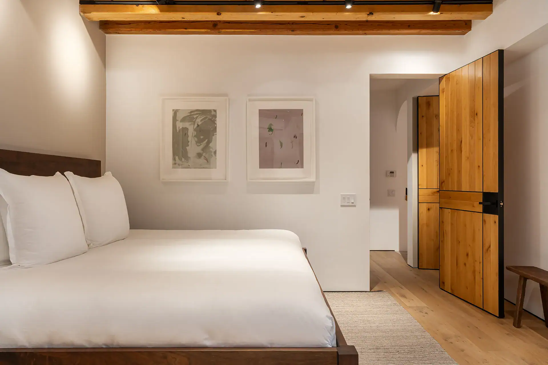 Villa del Parque Central, bedroom with a low bed, framed prints and a wood door under a beamed ceiling, San Miguel de Allende