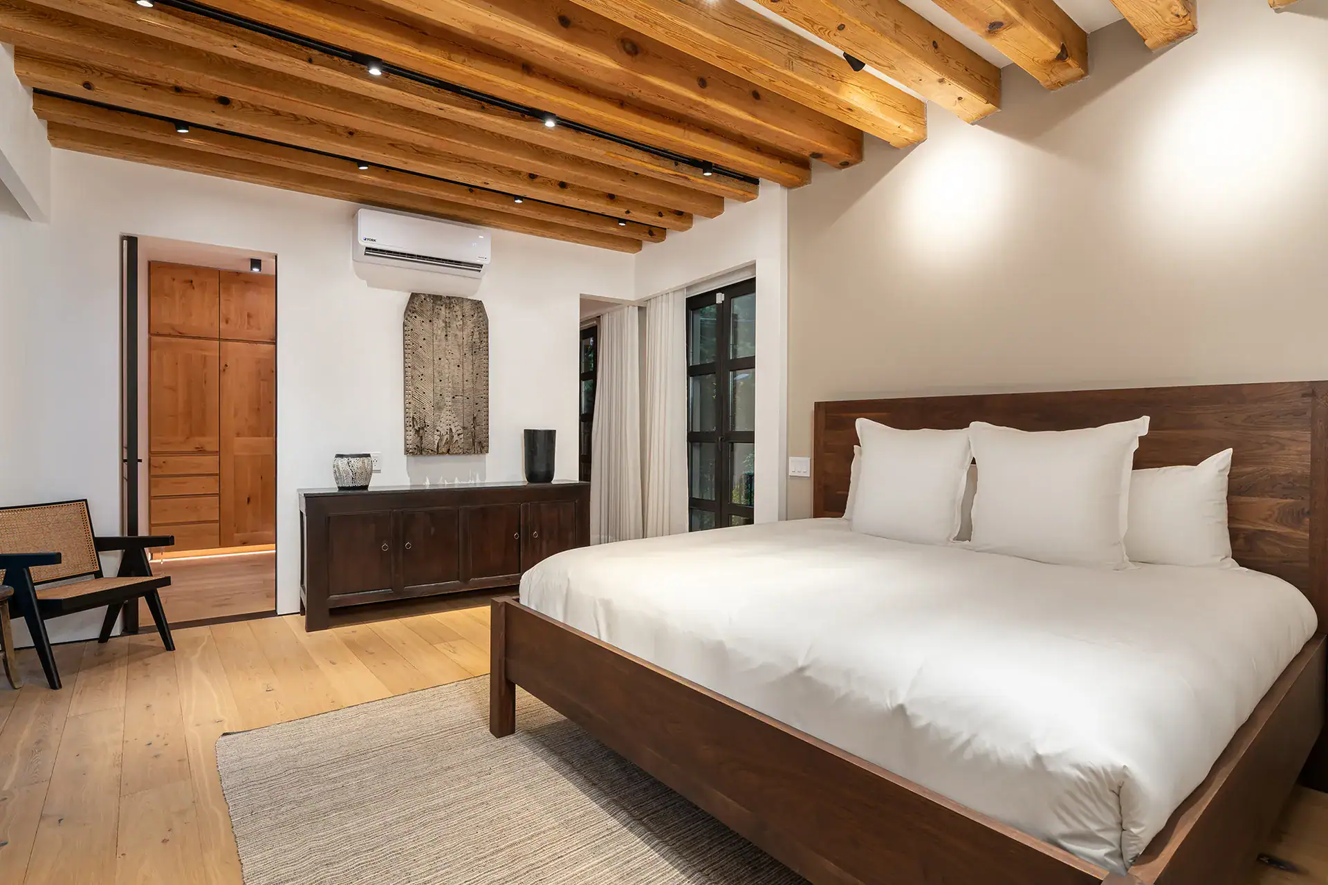 Villa del Parque Central, bedroom with a dark wood bed, sideboard and an armchair under a beamed ceiling, San Miguel de Allende