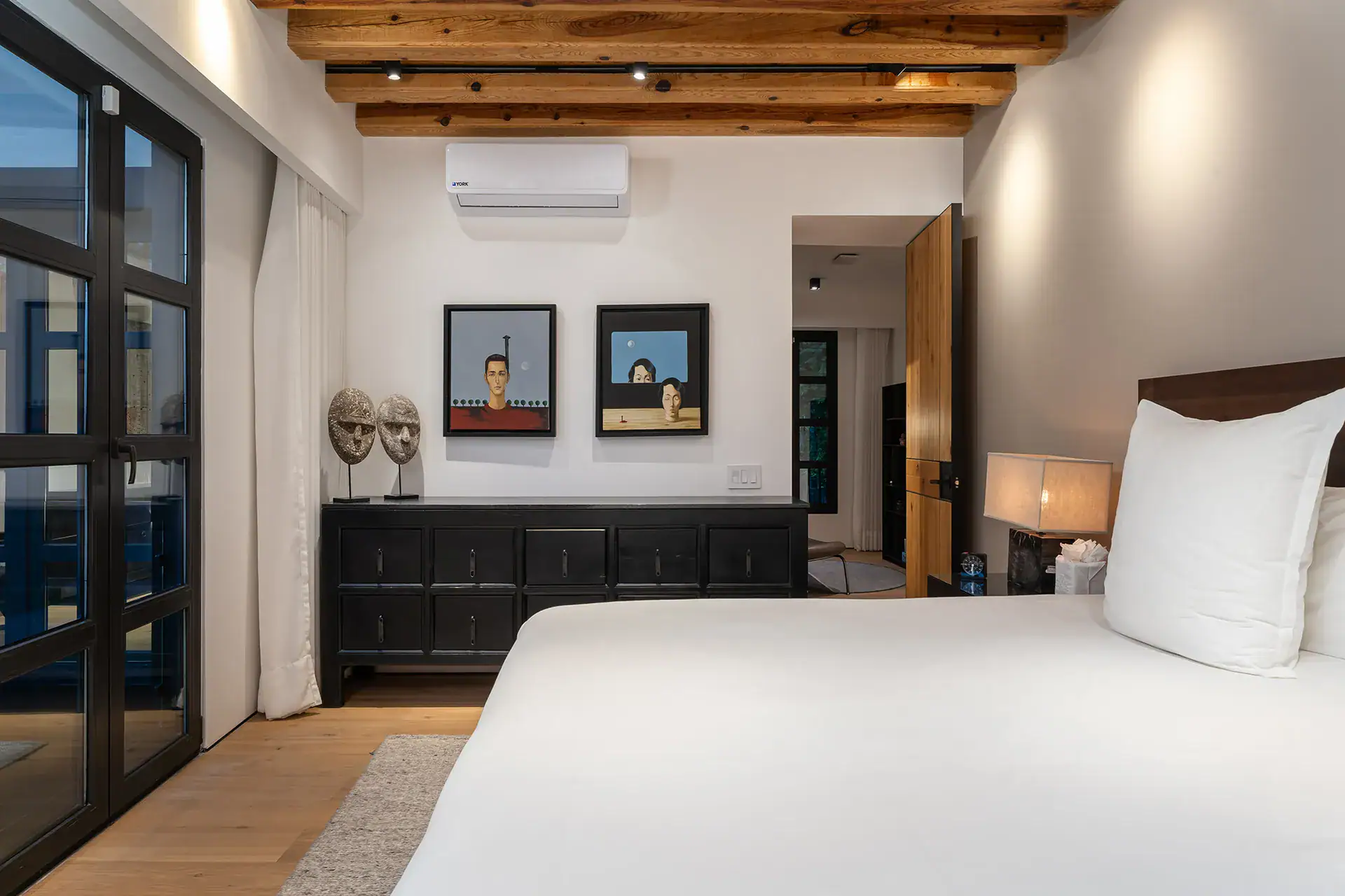 Villa del Parque Central, bedroom with a white bed, black sideboard, masks and a wall-mounted air conditioner, San Miguel de Allende
