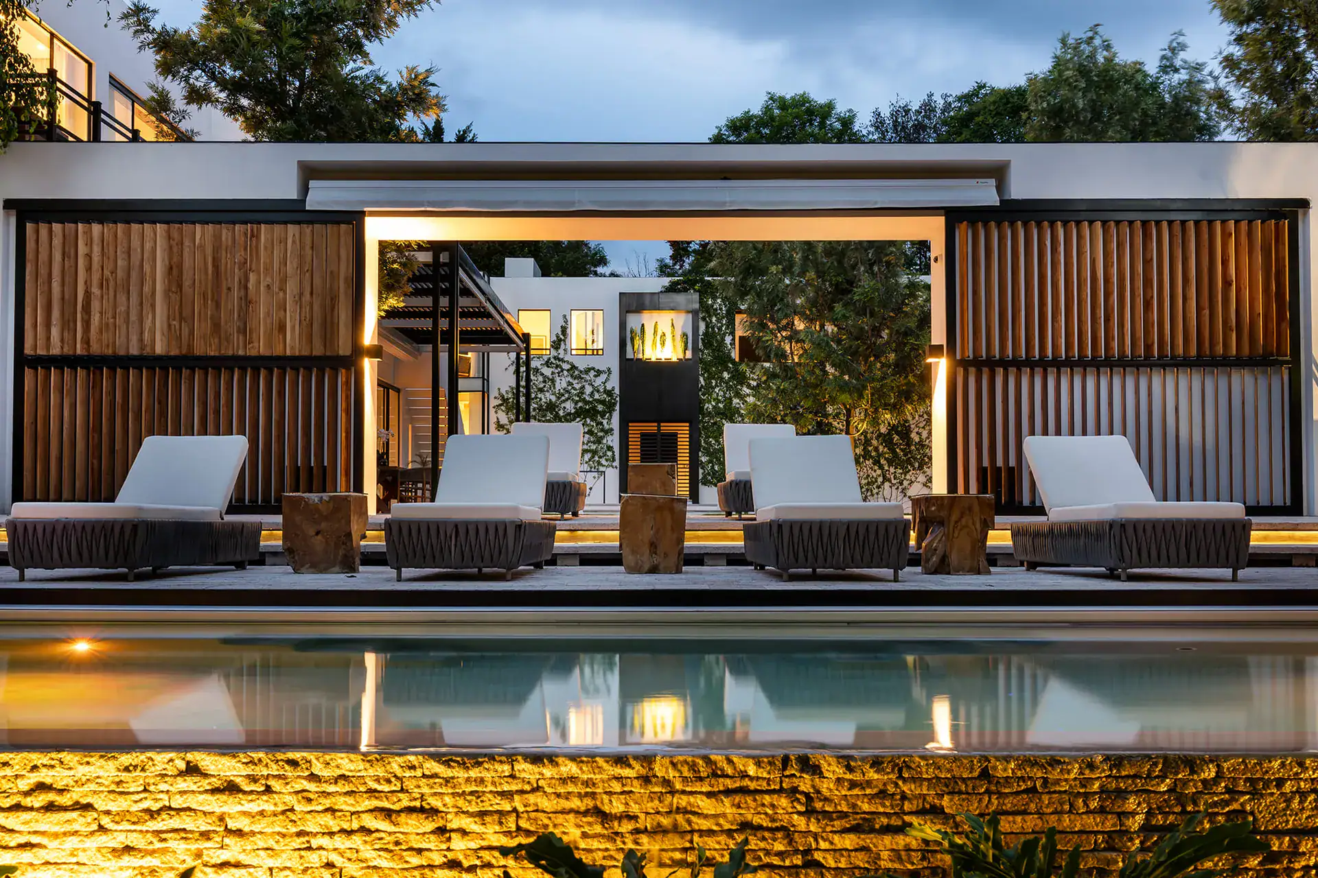 Villa del Parque Central, pool at dusk with lounge chairs and a glowing stone wall in front of a pavilion, San Miguel de Allende
