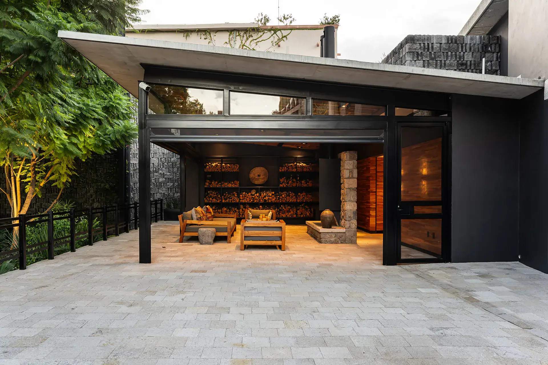 Villa del Parque Central, black-framed pavilion with seating and stacked firewood beside a paved courtyard, San Miguel de Allende