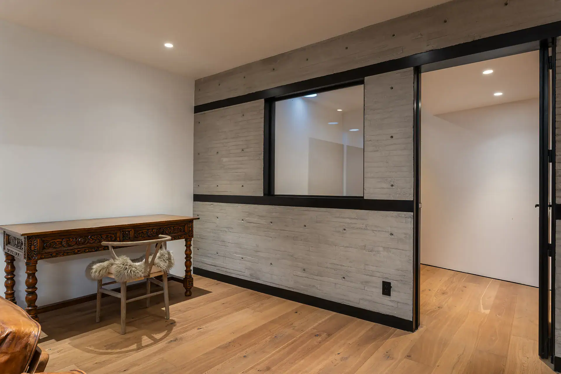 Villa del Parque Central, lower-level office room with a carved wood desk, oak floor and concrete-paneled wall, San Miguel de Allende