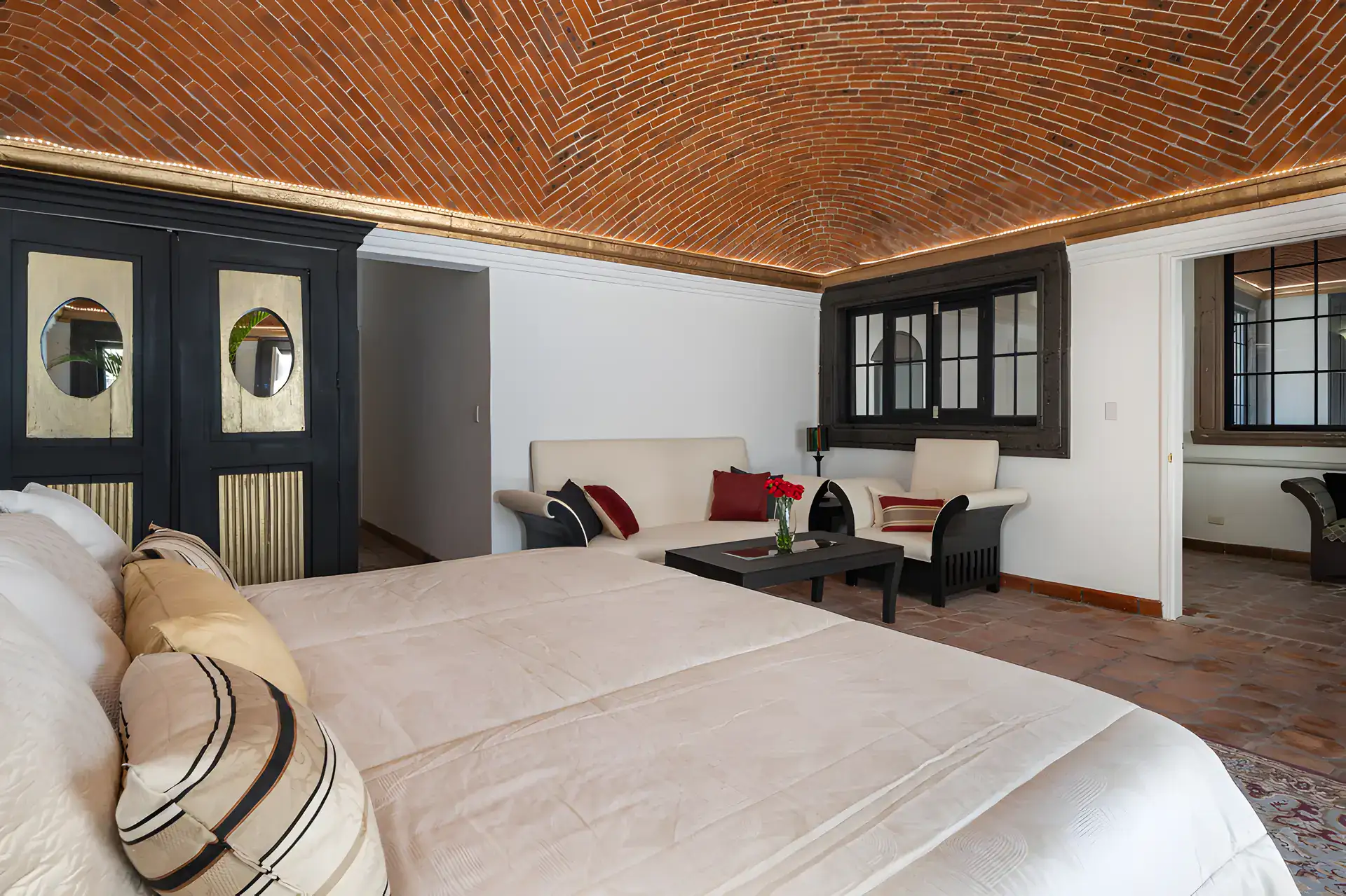 Villa Escondida, bed and a black armoire with round glass panels under a brick vaulted ceiling, San Miguel de Allende