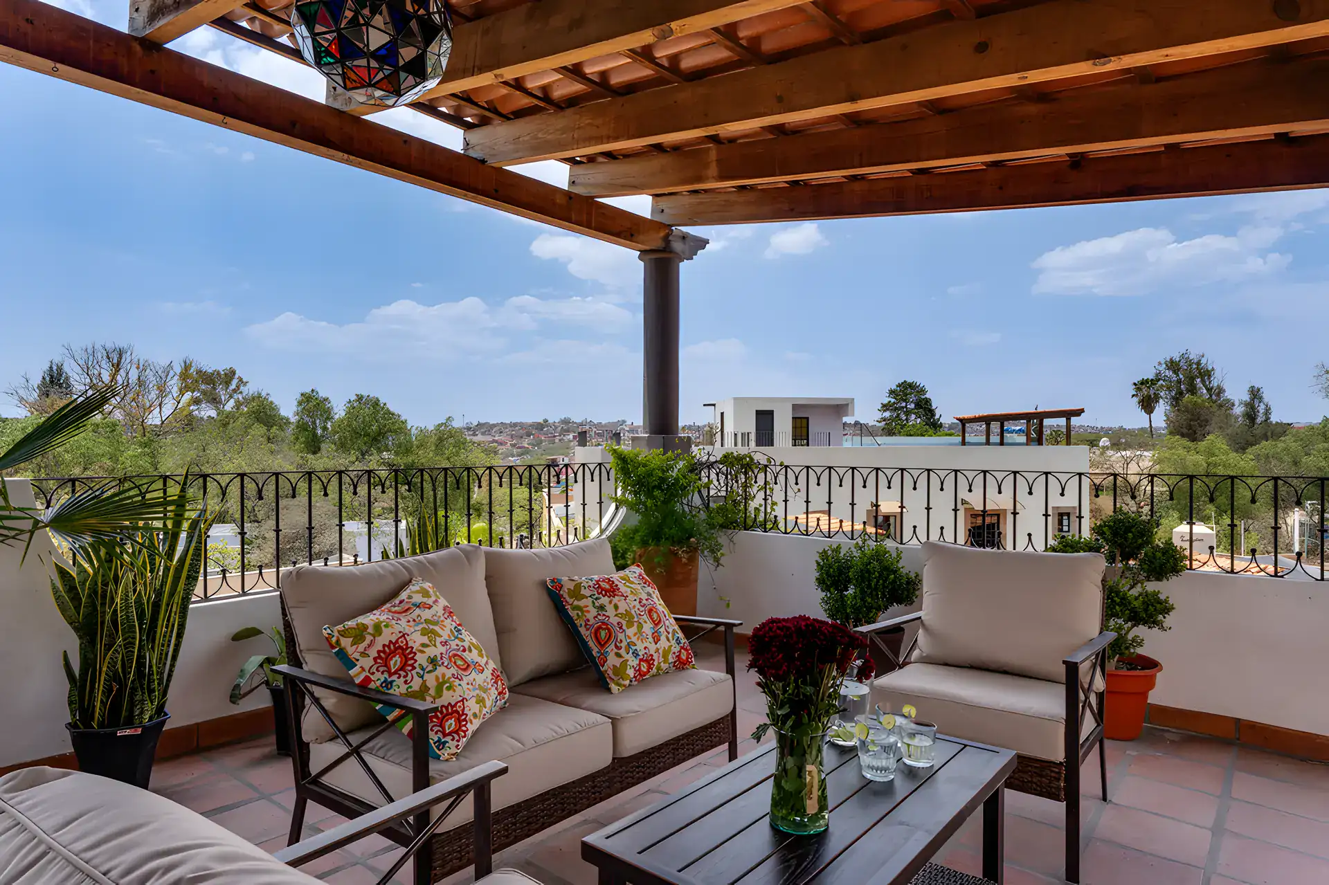 Villa Escondida, covered rooftop terrace with a rattan sofa, armchairs and a view of trees, San Miguel de Allende