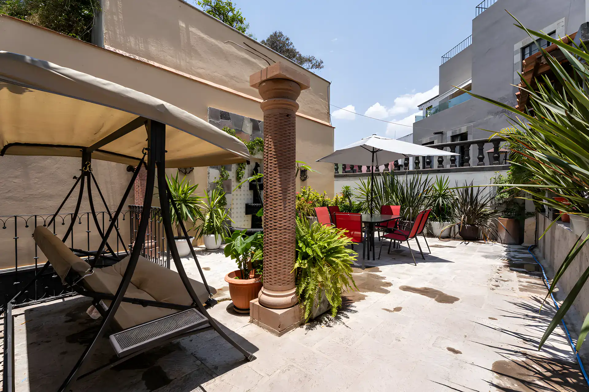 Villa Escondida, terrace with a covered swing, a stone column and a dining table with red chairs, San Miguel de Allende