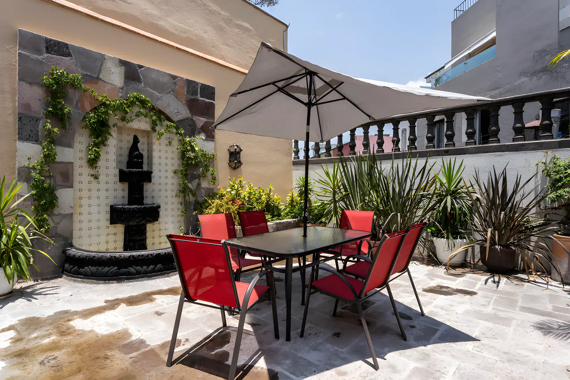 Villa Escondida, terrace dining table with red chairs in front of a tiled wall fountain, San Miguel de Allende